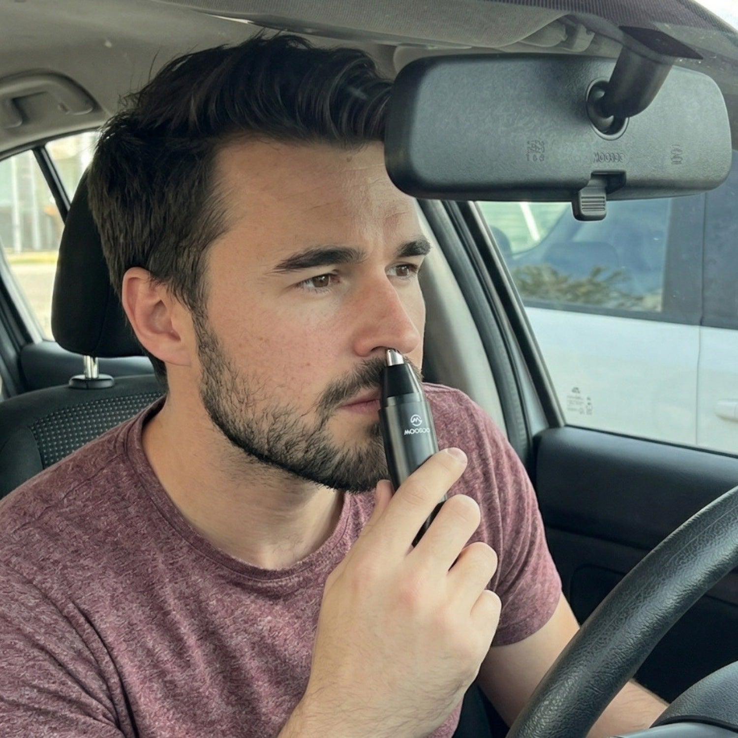Mann sitzt im Auto und verwendet einen elektrischen Nasenhaartrimmer für eine schnelle Pflege unterwegs.