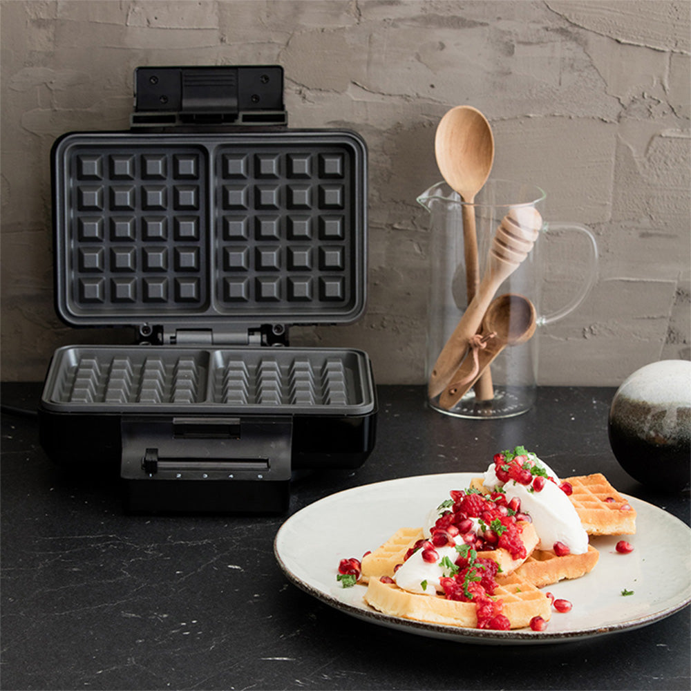Offenes Waffeleisen auf Küchenarbeitsplatte neben servierter Waffel mit Beeren und Sahne, ideal für frische Desserts oder Frühstück zuhause.